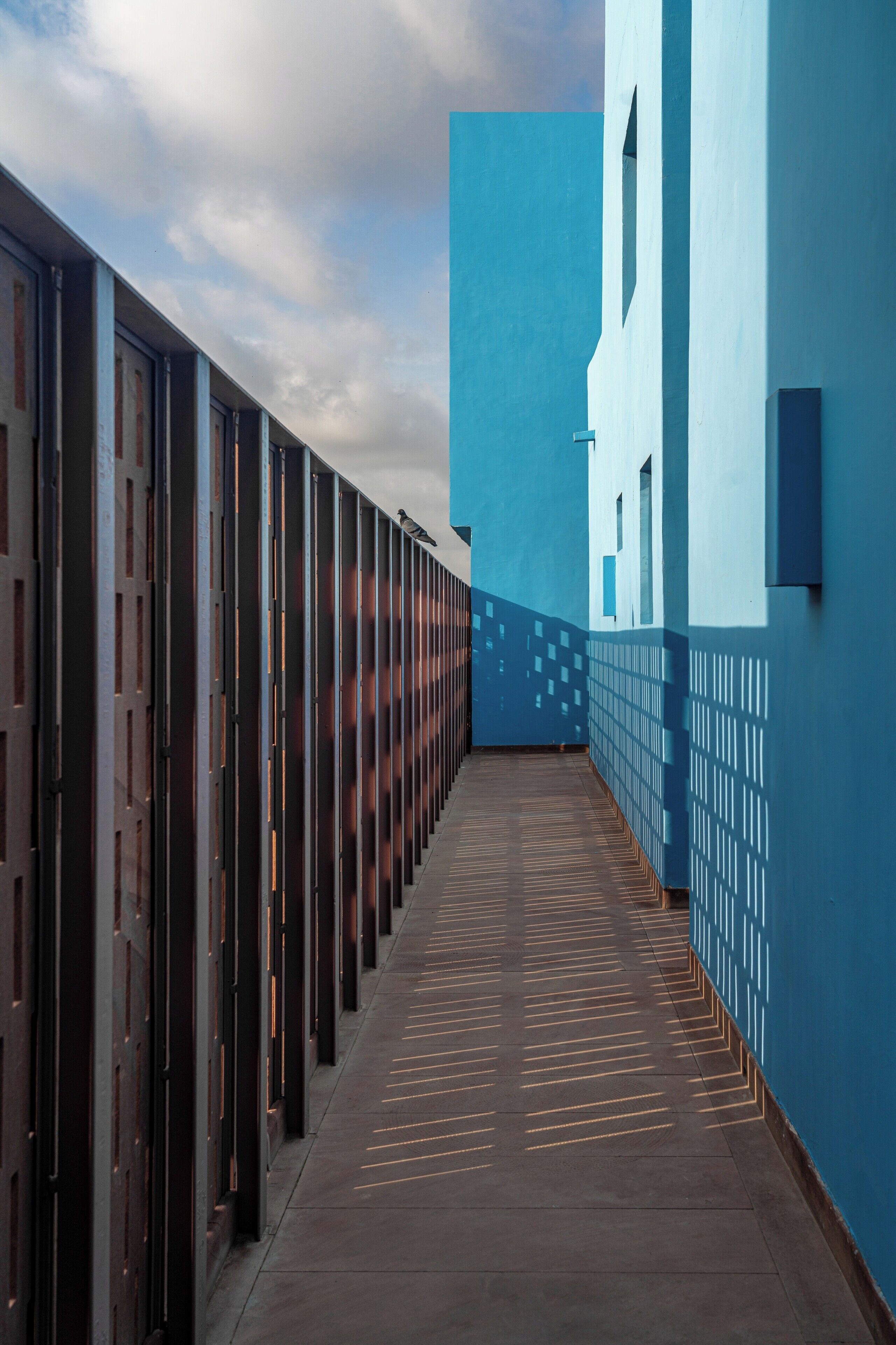 Um corredor com piso estampado, parede azul com design geométrico e grade de metal em um dos lados.