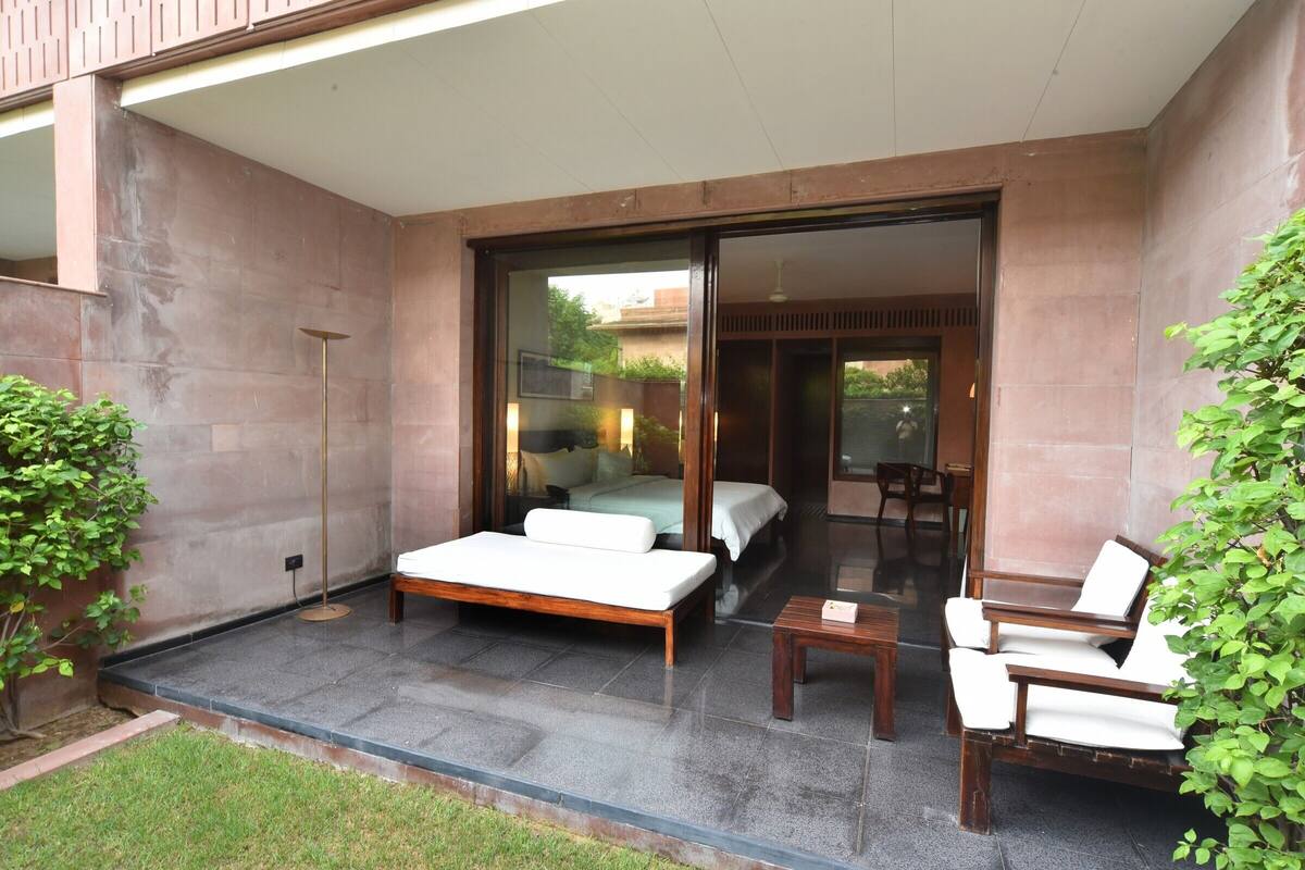 A modern outdoor living area with a sofa and chairs, a small table, and a glass door leading to a bedroom.