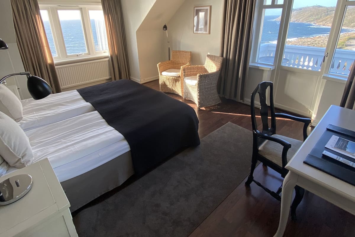 Une chambre d’hôtel avec un grand lit, un bureau, une chaise et une vue sur la mer.