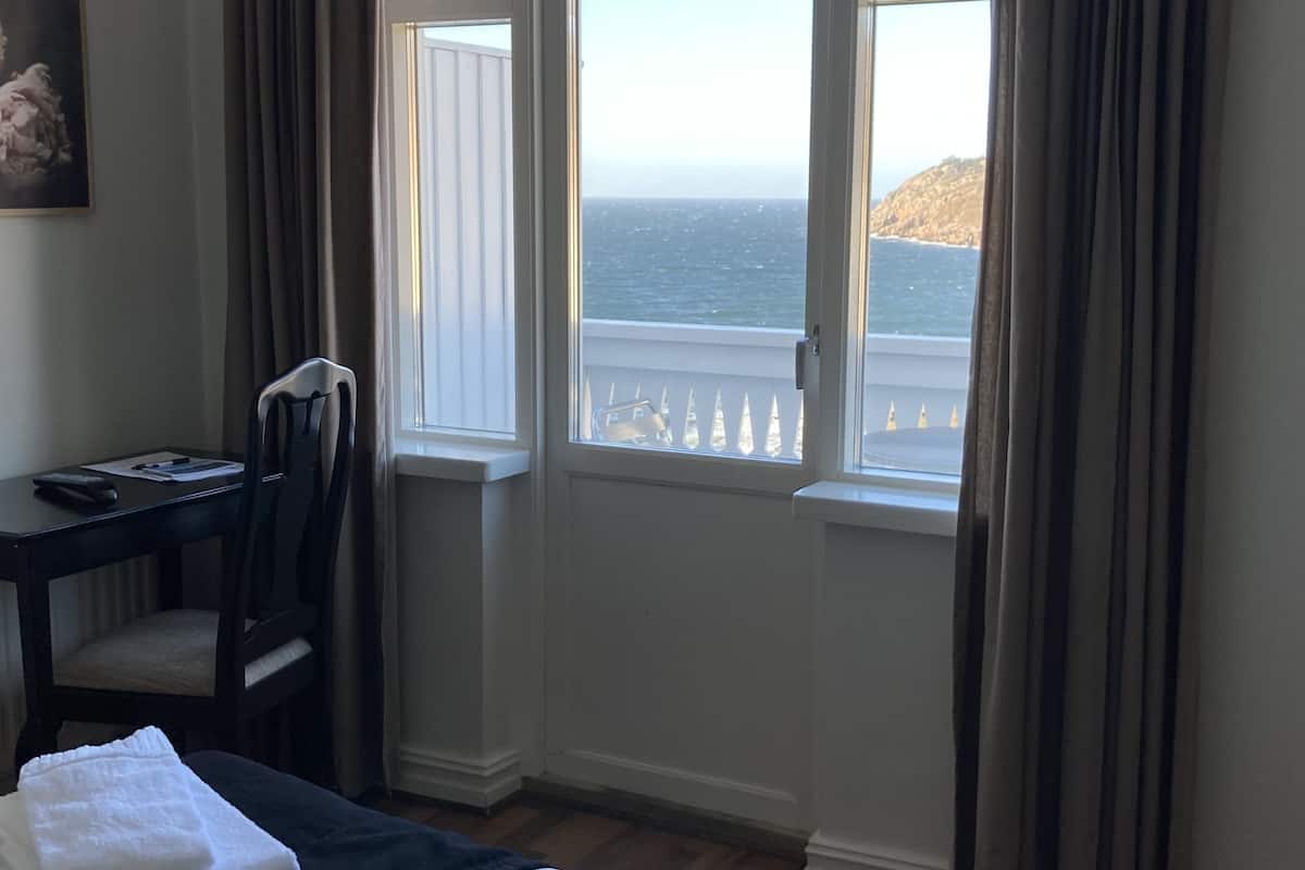 Une chambre d’hôtel avec un lit, un bureau, une chaise et une vue sur la mer par la fenêtre.