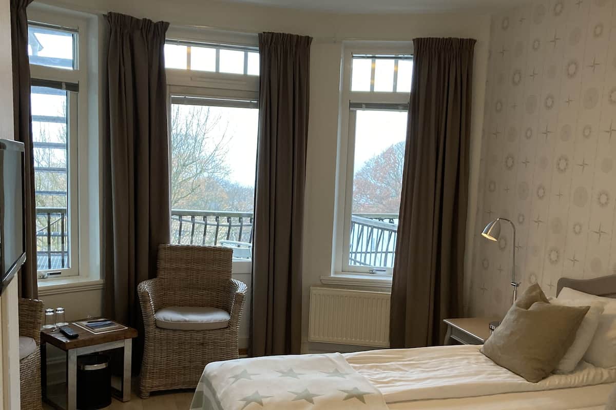 Une chambre d’hôtel avec deux lits, une chaise, une petite table, un téléviseur et de grandes fenêtres avec des rideaux.