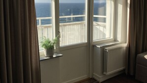 Une pièce dotée d’une grande fenêtre en arc de cercle donnant sur la mer, d’une plante en pot posée sur le rebord de la fenêtre et d’un radiateur.