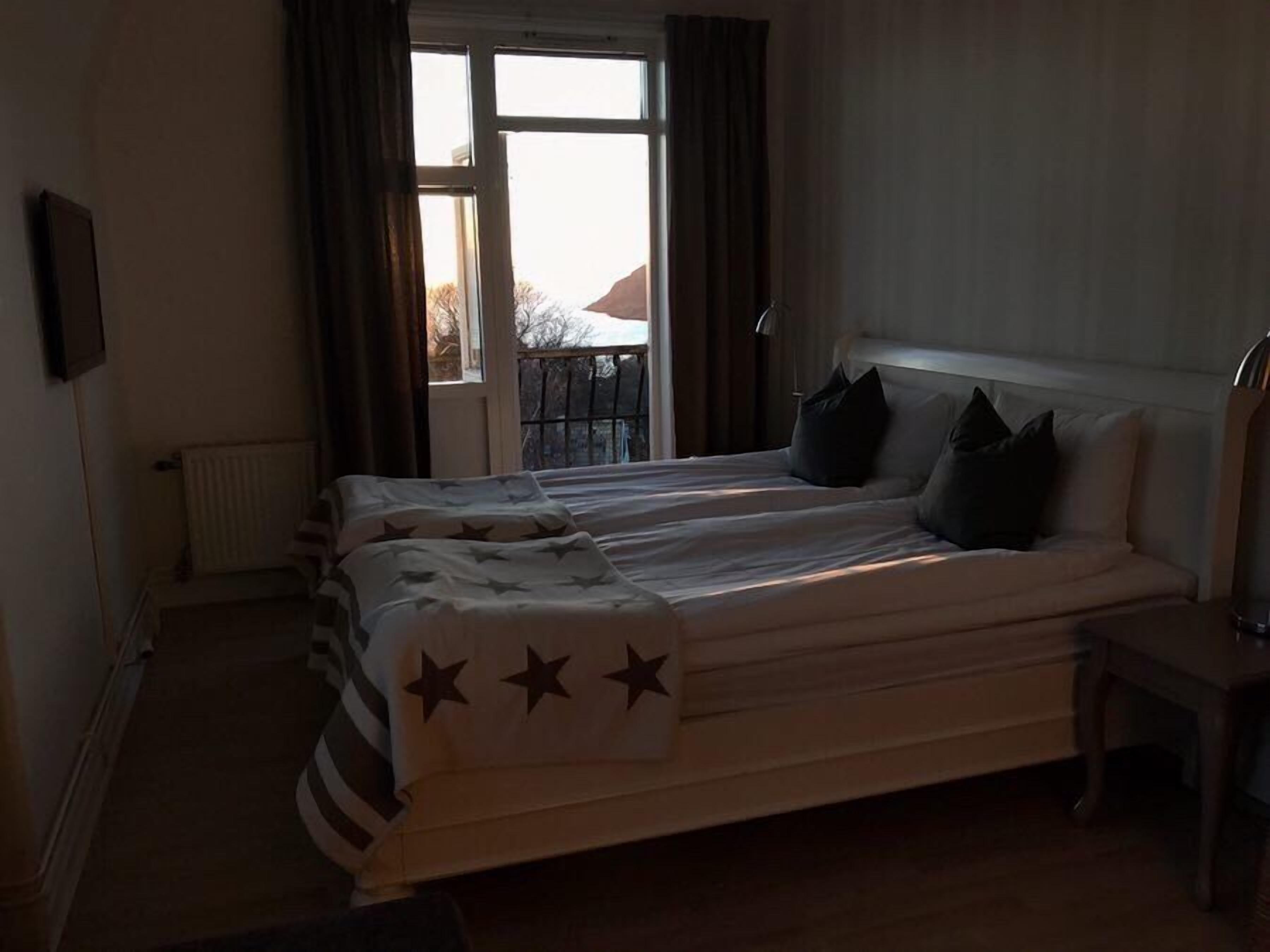 Et soveværelse med seng, stol, radiator og et vindue med gardiner.