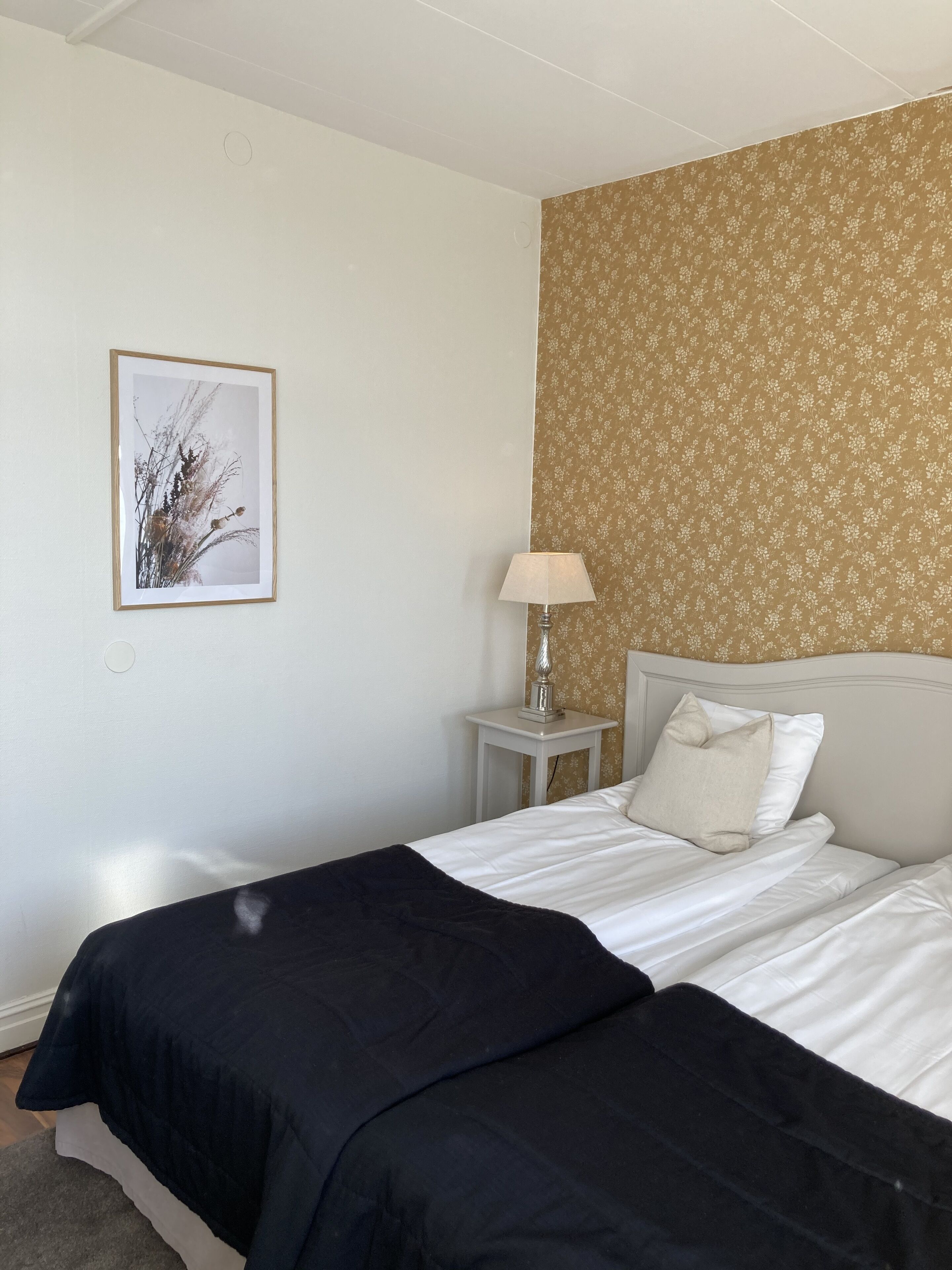 A hotel room with a bed, a nightstand, a lamp, and a framed picture on the wall.