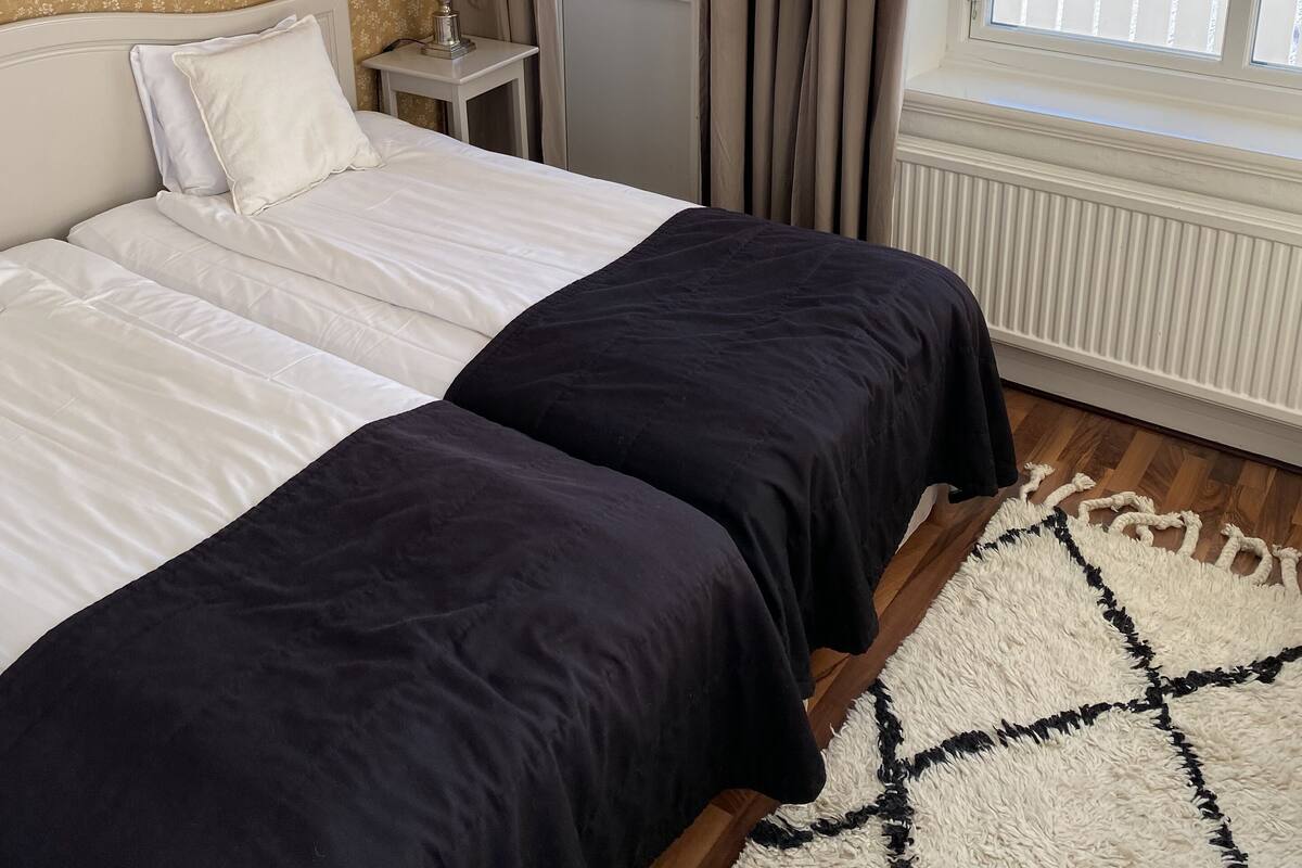 Une chambre à coucher avec un lit, une table de chevet, une lampe, une fenêtre avec des rideaux et une vue sur la mer.