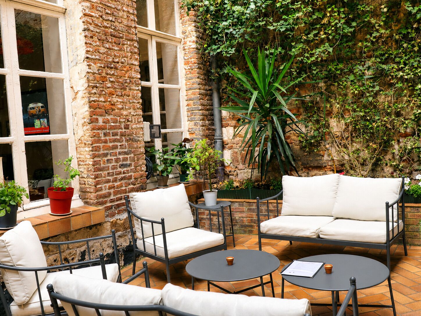 An outdoor seating area with brick walls, potted plants, and a large green plant in the center.