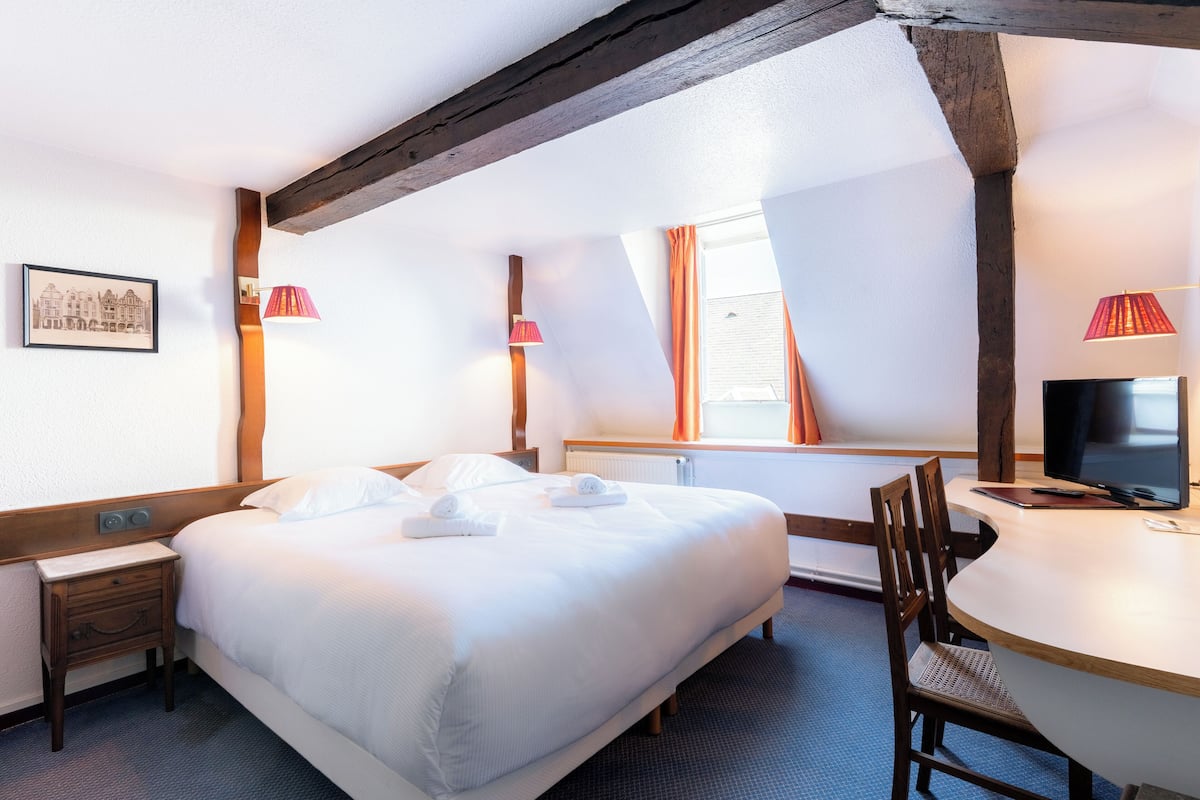 Una habitación de hotel con una cama grande, un escritorio, una silla, un televisor y una ventana con cortinas.