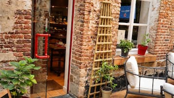 Een terras met buitenmeubilair, een bakstenen muur, een houten ladder en potplanten.