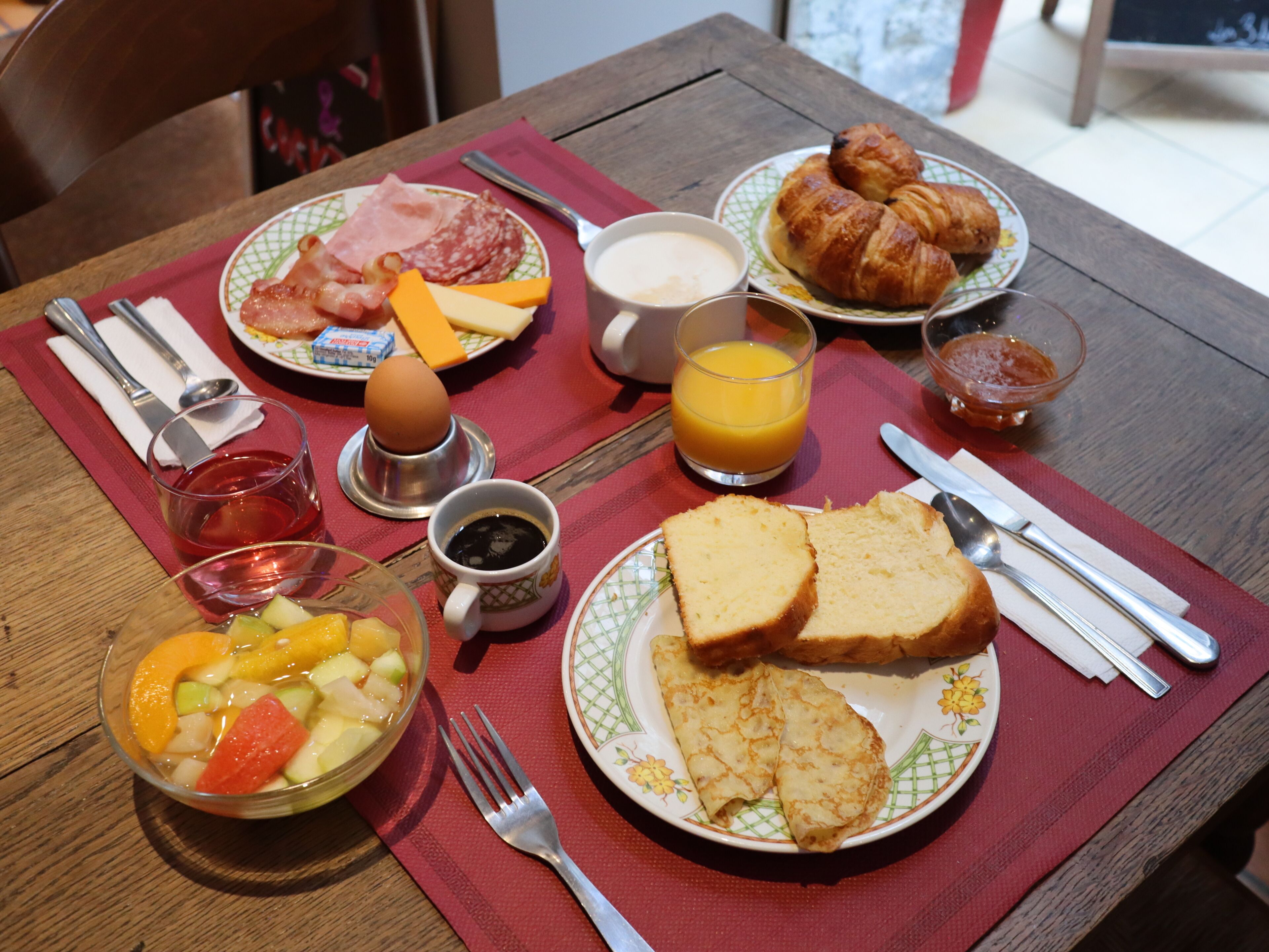 A breakfast table with plates of food, a fruit bowl, a glass of orange juice, and a cup of coffee.