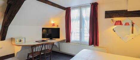 A hotel room with a bed, a desk with a computer, a chair, and a window with curtains.
