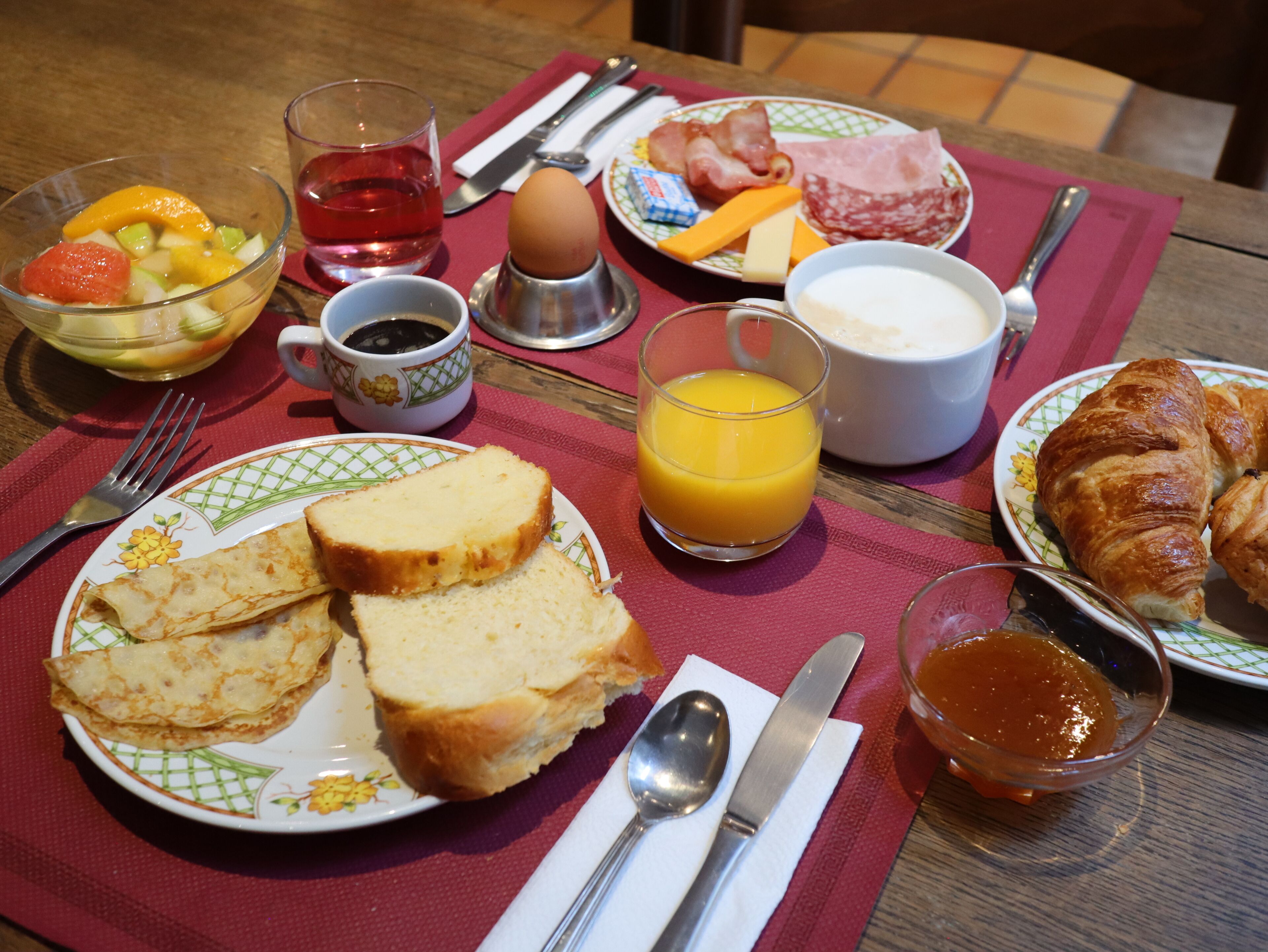 A breakfast table with plates of food, a glass of orange juice, a cup of coffee, and a croissant.