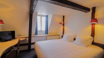 Quarto de hotel com uma cama, uma mesa de trabalho com uma televisão e duas luminárias.