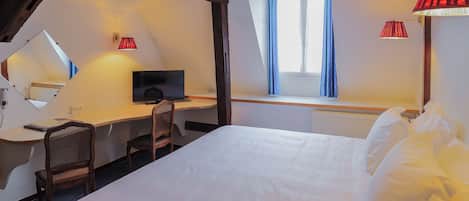 Habitación de hotel con cama, escritorio, silla, televisor y ventana con cortinas.