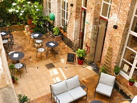Un patio al aire libre con paredes de ladrillo, varias mesas y sillas, plantas en macetas y una bicicleta.