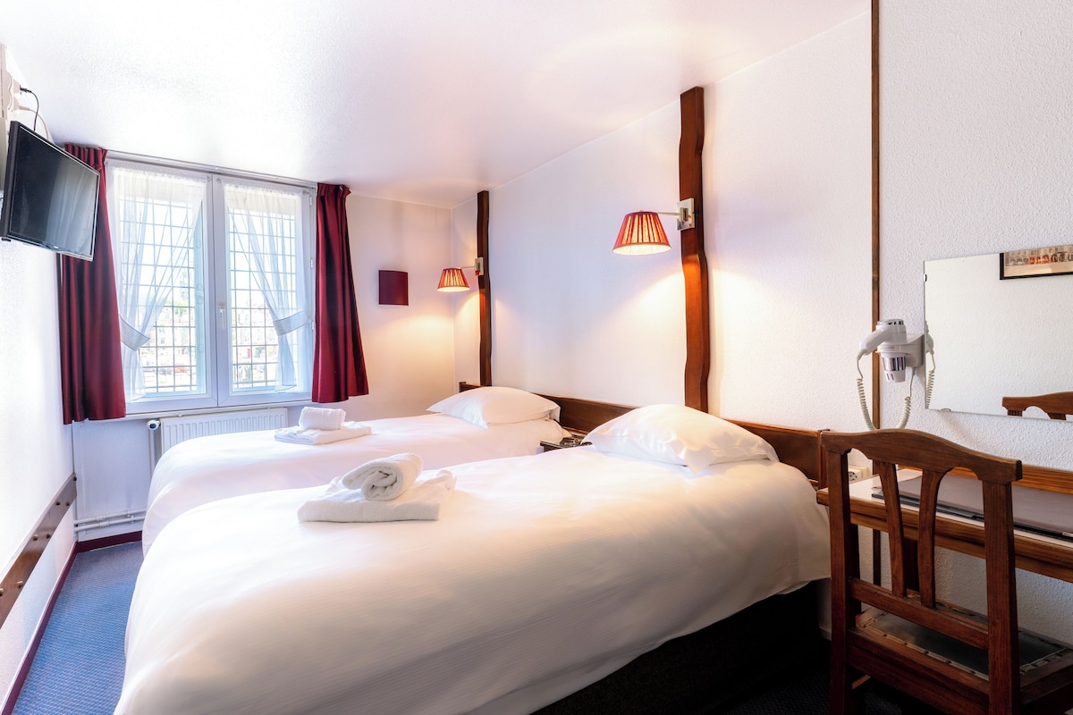 Habitación de hotel con dos camas, televisión, escritorio con teléfono y ventana con cortinas.