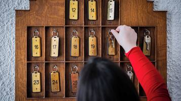 A wooden key rack with numbered compartments, a hand reaching for a key.