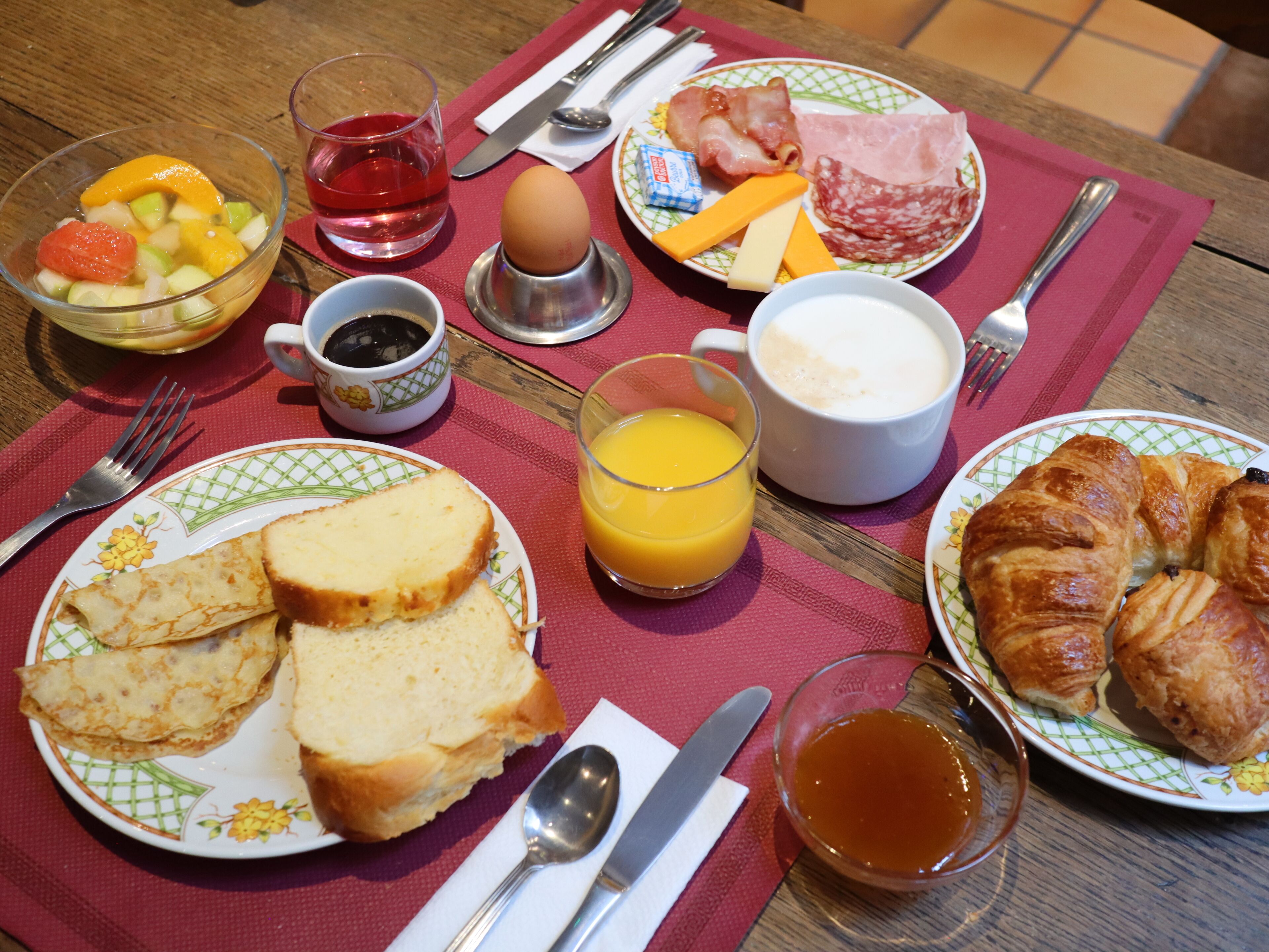 Een ontbijttafel met borden vol eten, een glas sinaasappelsap, een kop koffie en een croissant.