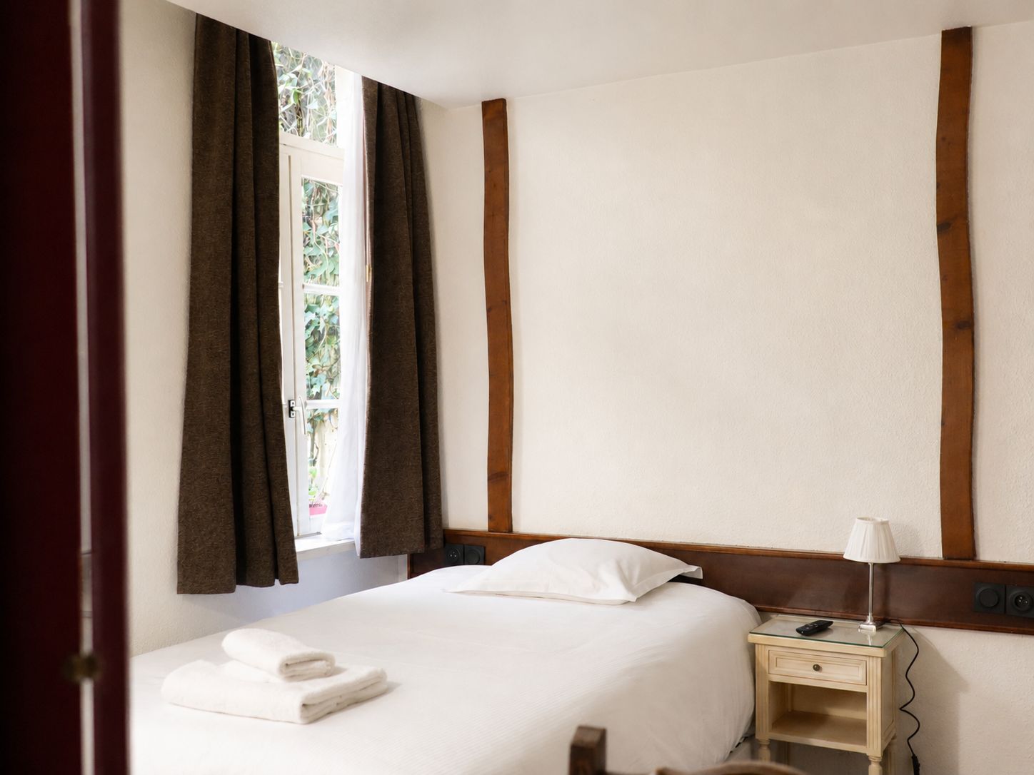 Una habitación de hotel con cama, mesita de noche, lámpara y ventana con cortinas.