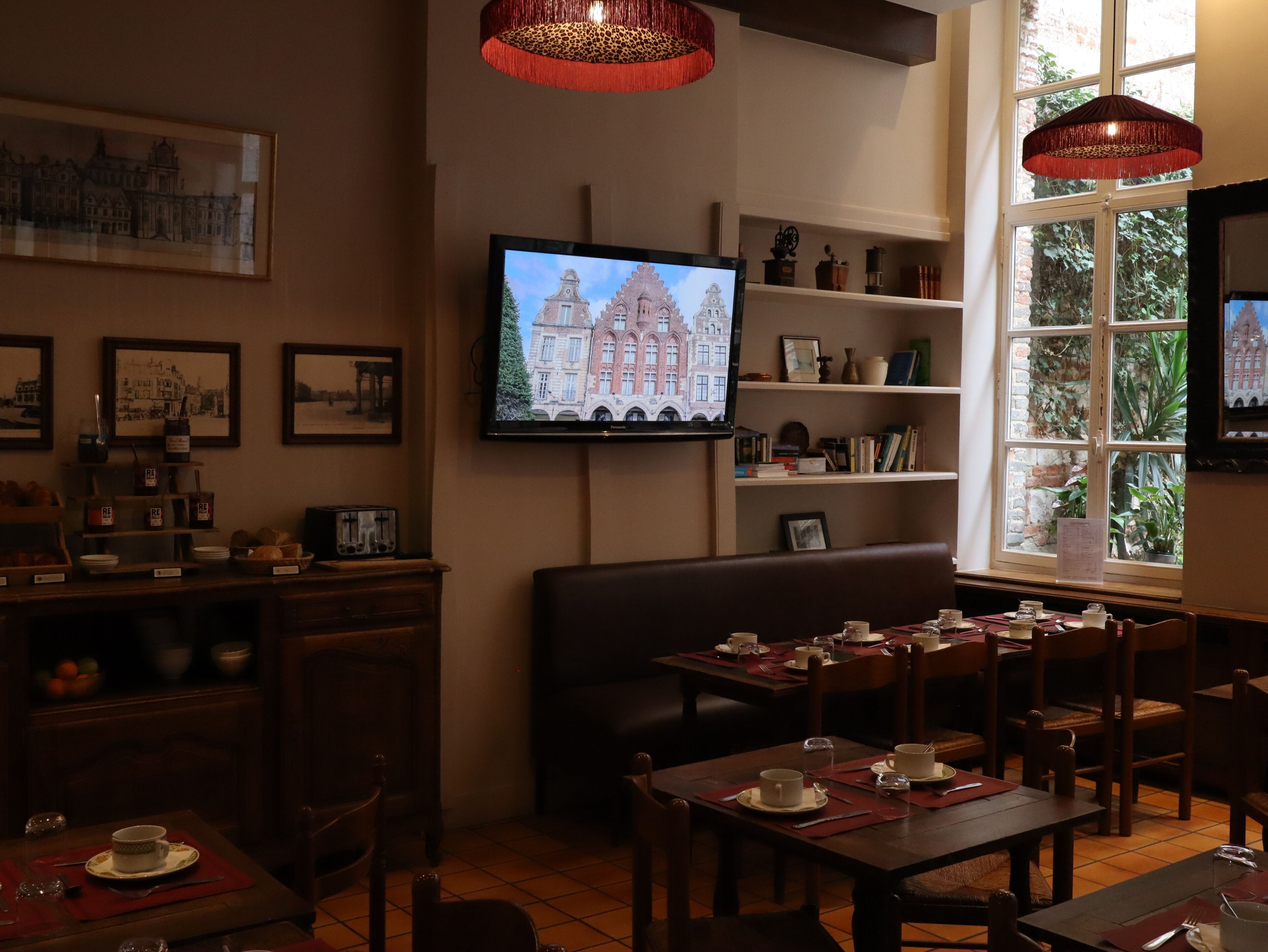 A cozy dining area with tables set for tea service, a television mounted on the wall, and framed pictures on the wall.