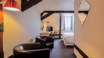 A hotel room with a bed, two chairs, a desk, a TV, and a mirror.