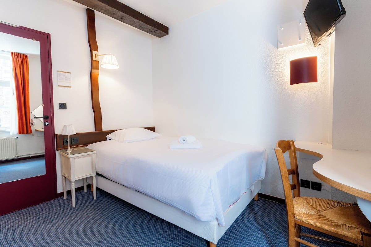 Habitación de hotel con cama, mesita de noche, silla y televisión instalada en la pared.