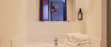 A bathroom with a white sink, a mirror, a towel stack, and a bottle of hand soap.