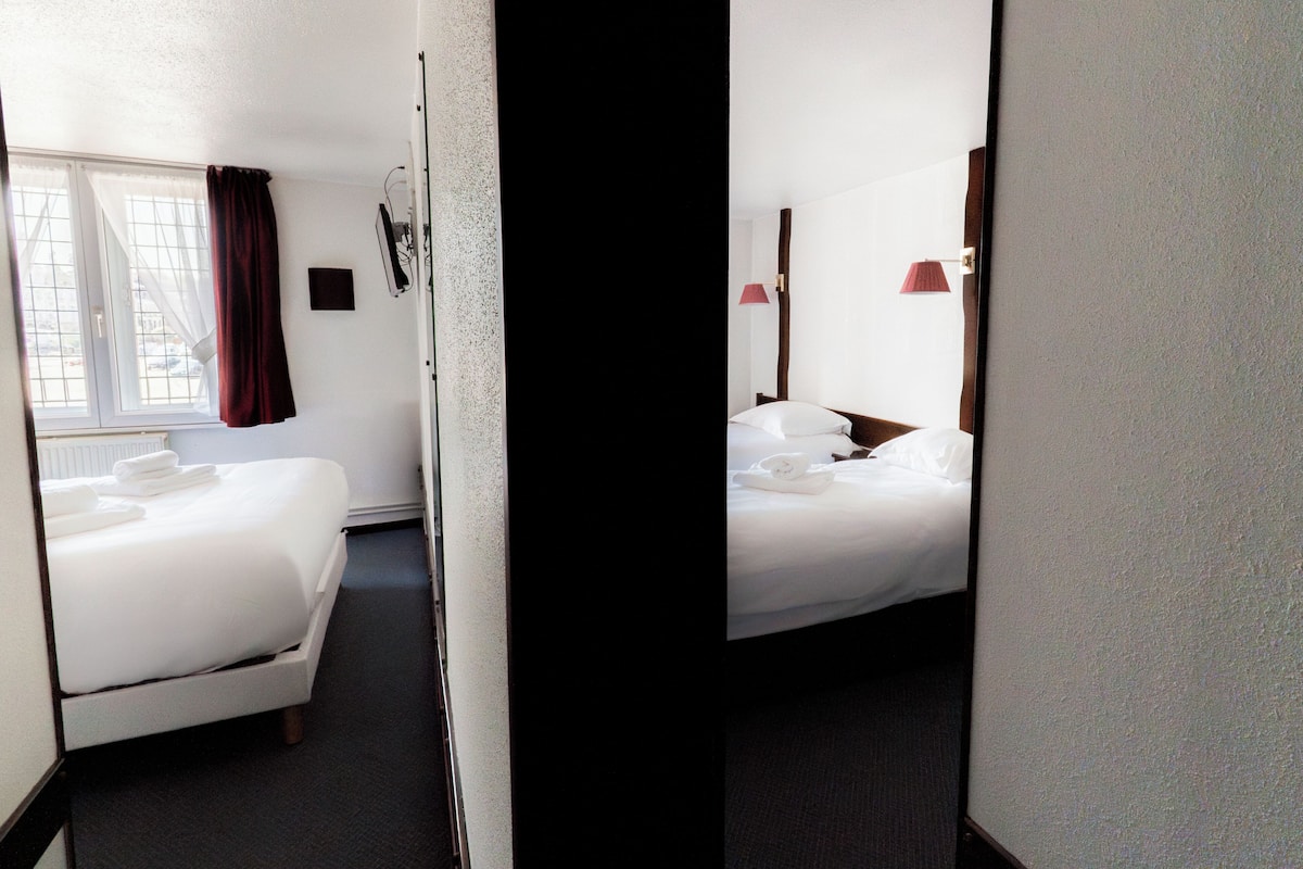 Una habitación de hotel con una cama, una ventana con cortinas, una mesita de noche y una lámpara.