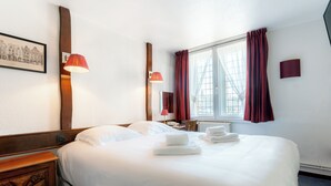 Een hotelkamer met een groot bed, een houten nachtkastje, een nachttafeltje met een lamp, een raam met gordijnen en een lijst met een afbeelding aan de muur.