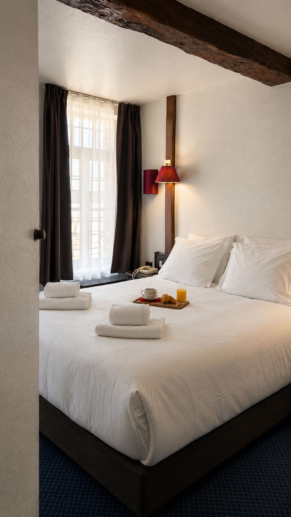 Una habitación de hotel con una cama, una mesita de noche, una lámpara y una ventana con cortinas.