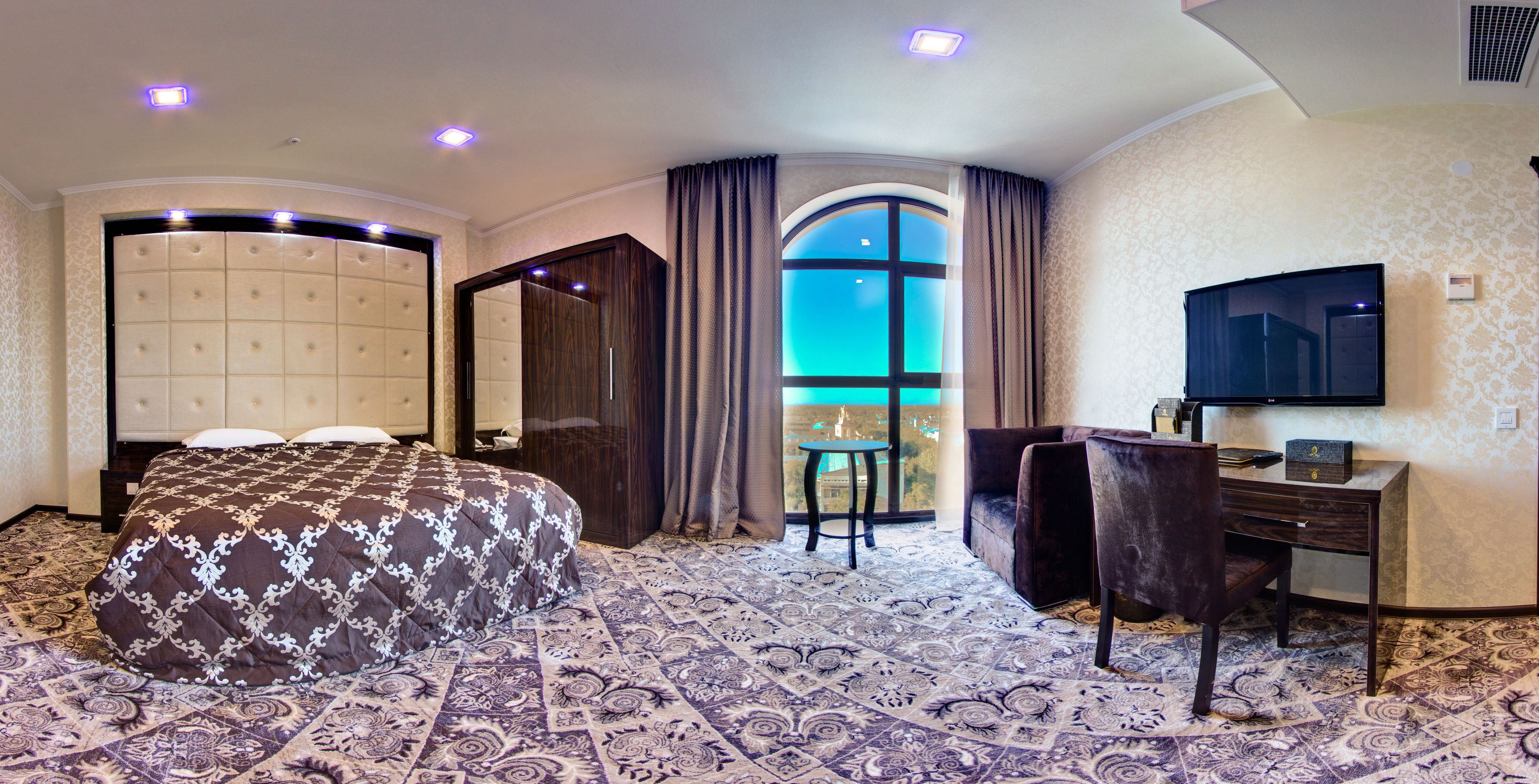 Une chambre d’hôtel avec un grand lit, un bureau avec une chaise, une télévision et une vue sur la ville grâce à une grande fenêtre.