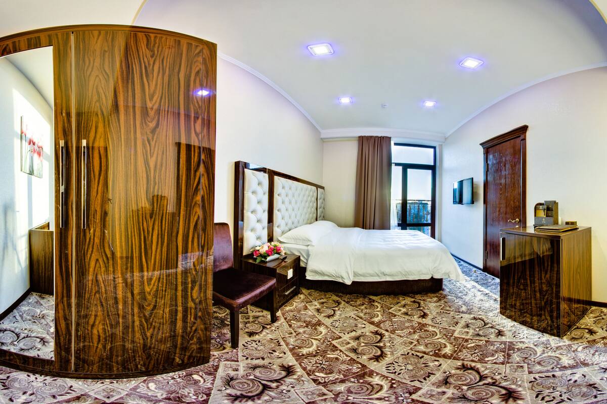 Une chambre d’hôtel avec un grand miroir, un lit recouvert d’une couette blanche, une armoire en bois et un petit bureau avec un téléviseur.