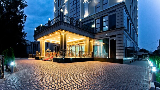 Ein Hotel mit Eingangsbereich, einem Kopfsteinpflaster-Zugangsweg, einer überdachten Vorfahrt und einem Balkon mit Geländern.