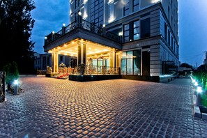 Een hotelentree met een geplaveid pad, een overdekte inkomhal en een balkon met hekwerken.