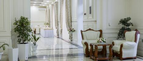 A spacious lobby with a polished marble floor, elegant white furniture, and decorative plants.