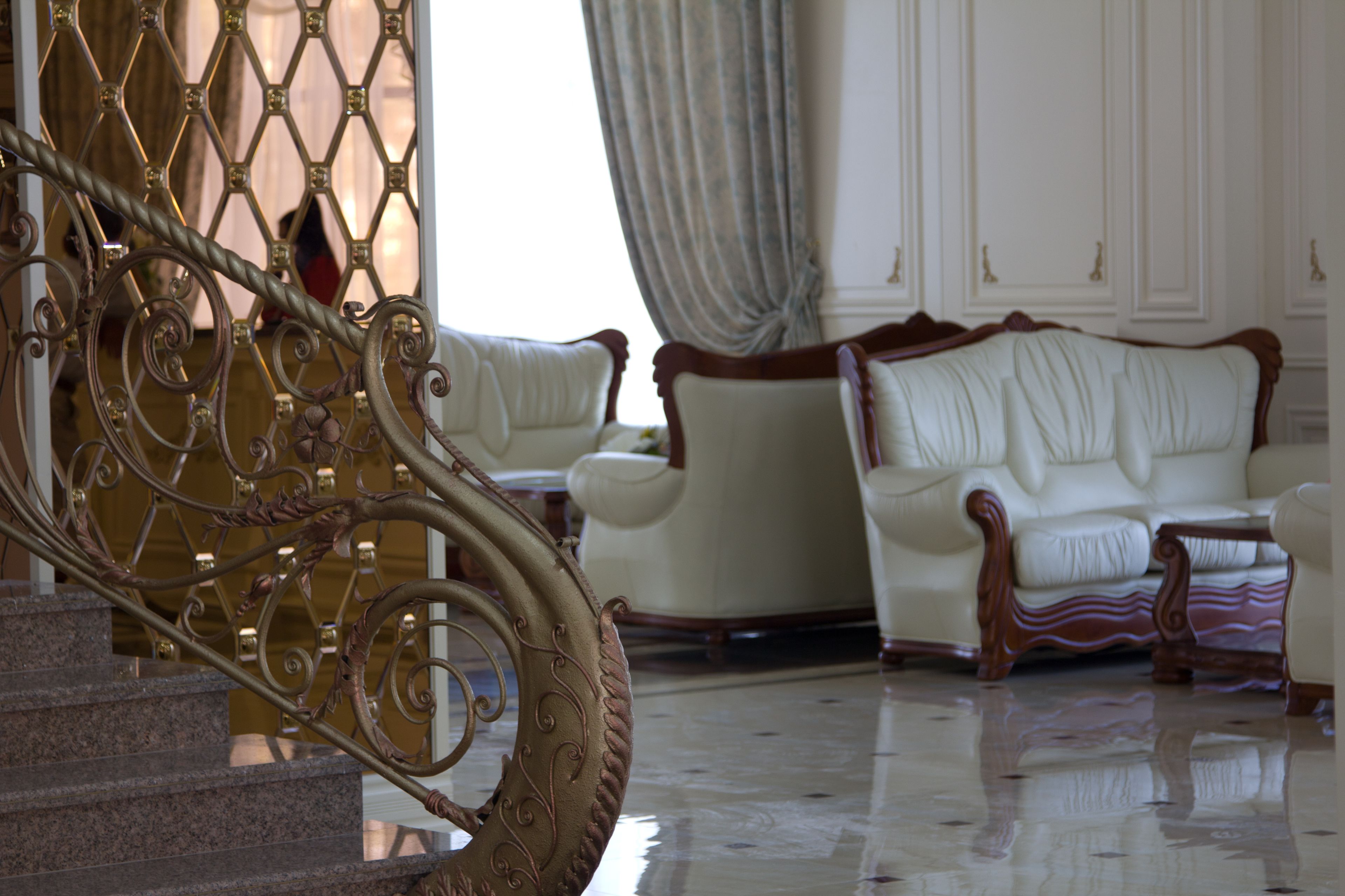 Una imponente escalera con barandillas de metal ornamentado que conduce a un espacio de descanso con sofás blancos de cuero suave y un suelo de mármol pulido.