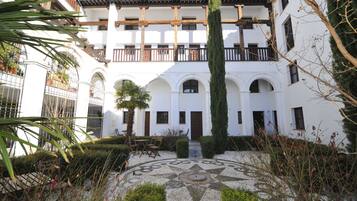 A courtyard with a tiled floor, a wooden bench, and a tall cypress tree.