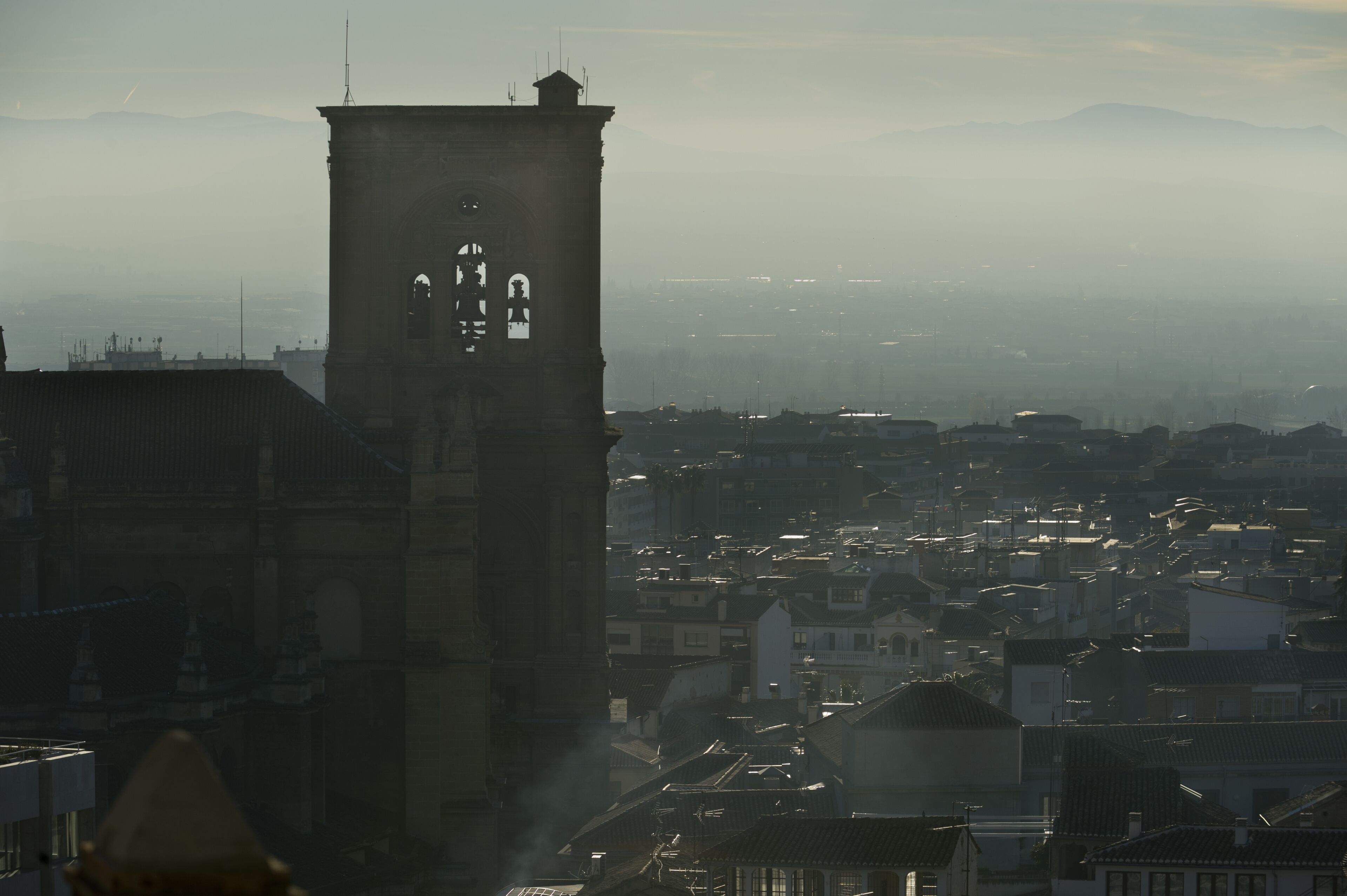 Una torre con un orologio e vista su una città, con edifici e montagne sullo sfondo.