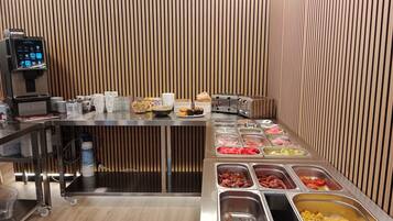Buffet montado com diversos alimentos, uma máquina de café e uma torradeira.