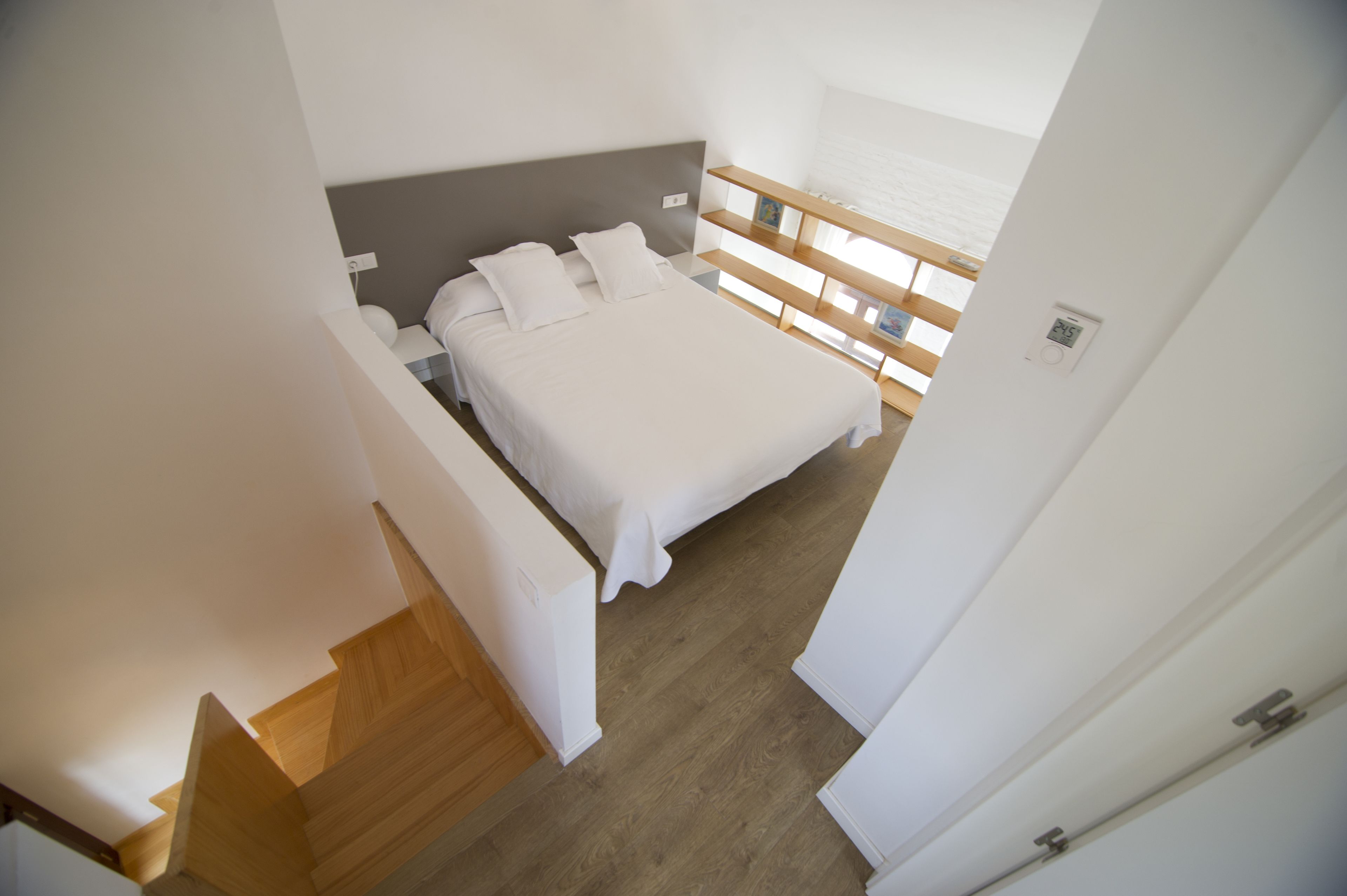 Un dormitorio con cama, cabecero de madera, ropa de cama blanca y una ventana con persianas.