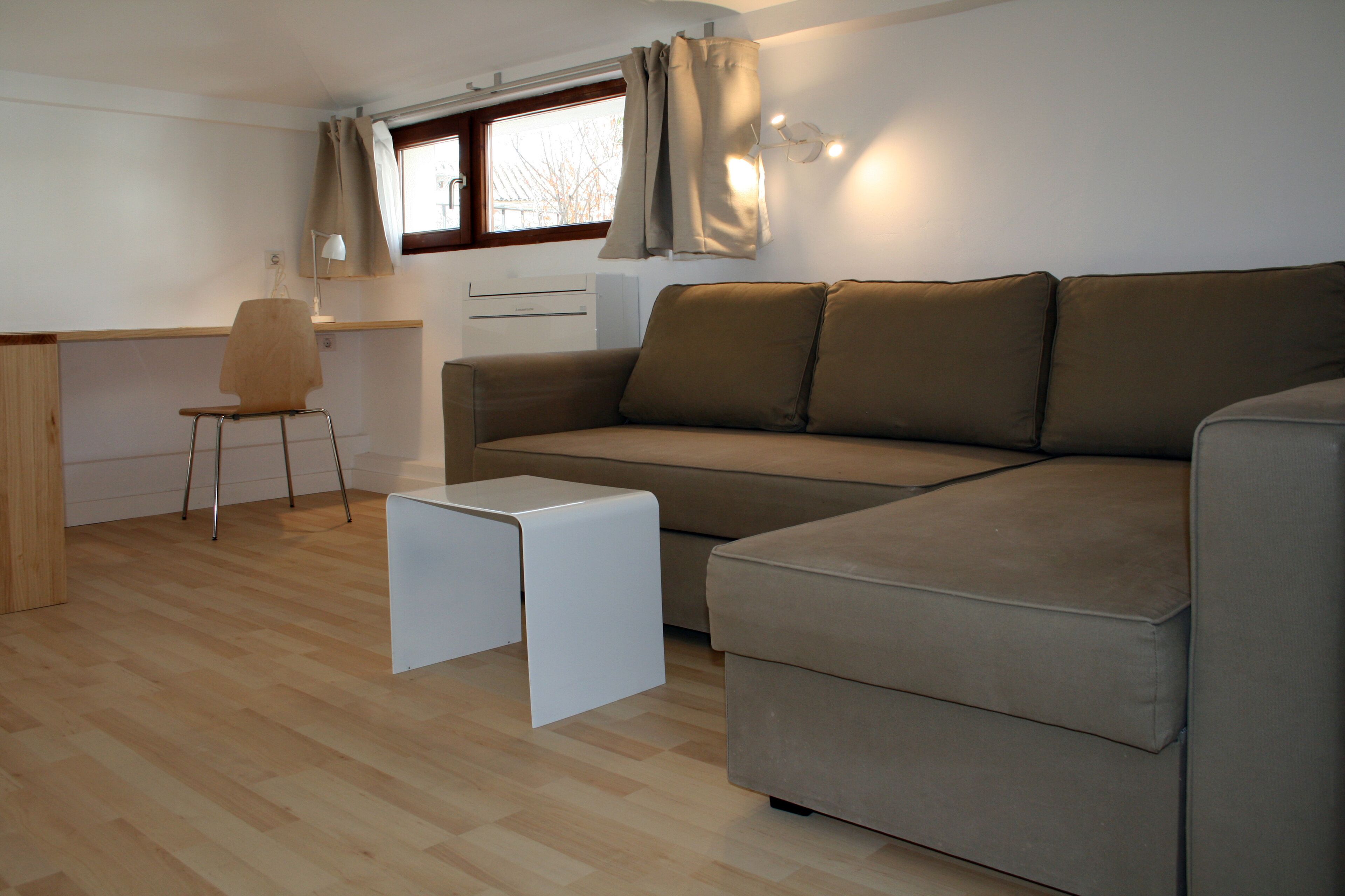A compact living space with a sofa, a small table, a chair, and a desk area.