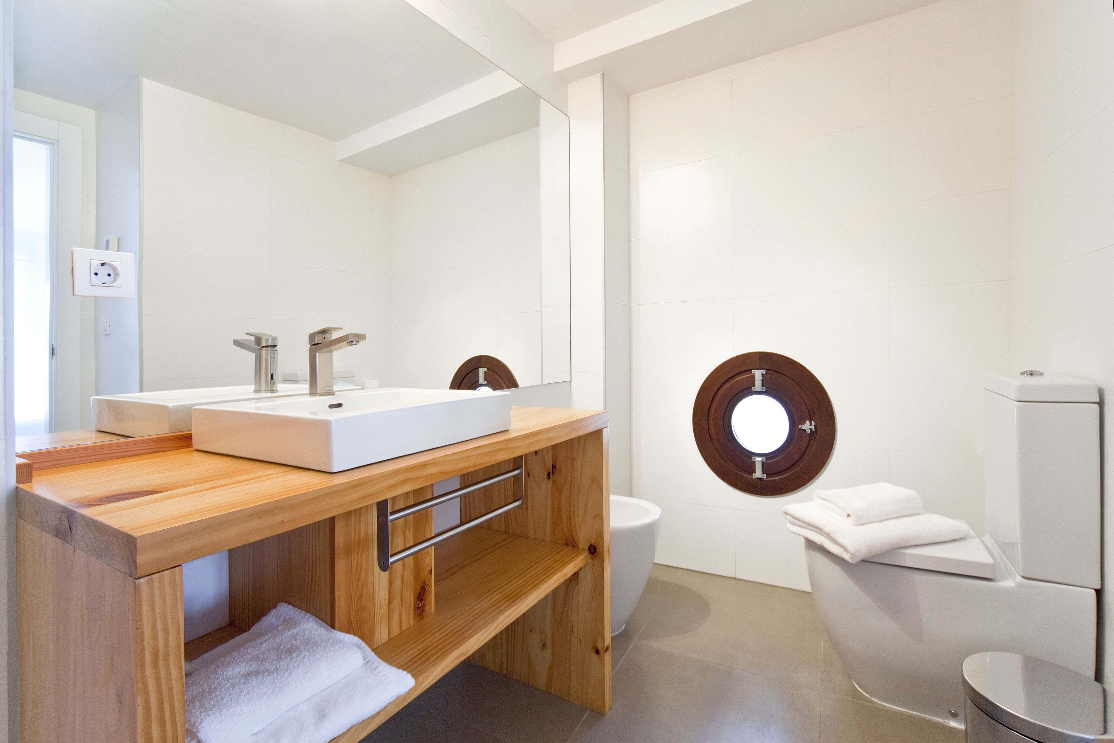 A modern bathroom with a wooden vanity, two sinks, a toilet, and a bidet.