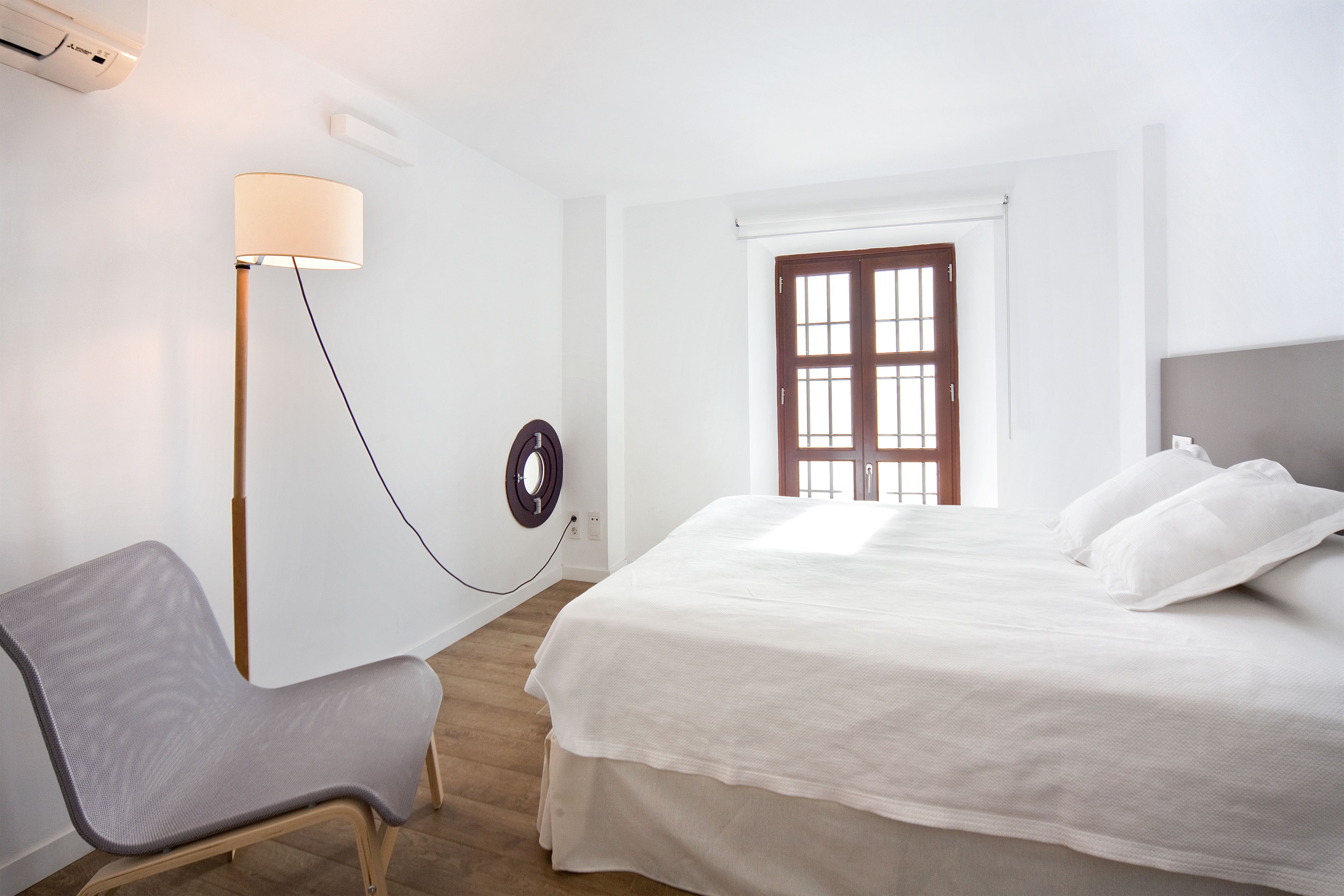 A bedroom with a bed, a chair, a lamp, and a window.