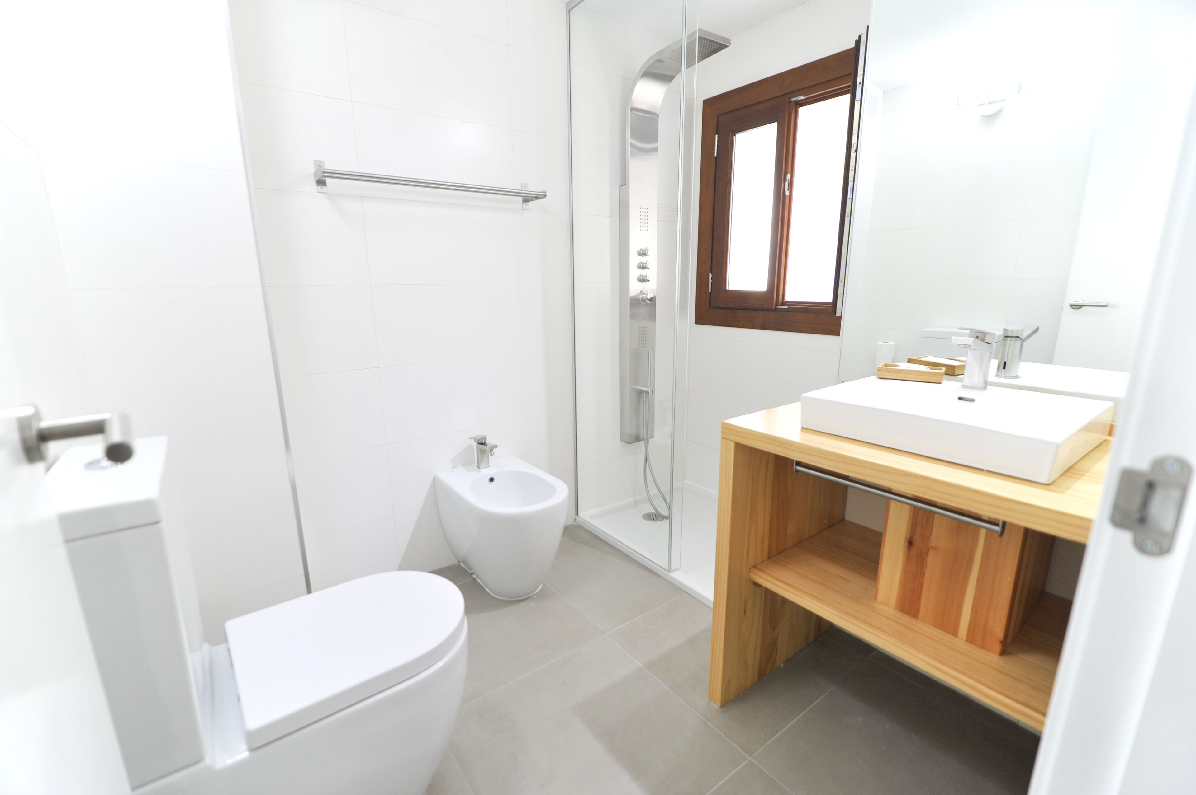 A modern bathroom with a shower, toilet, bidet, and a vanity with a mirror.
