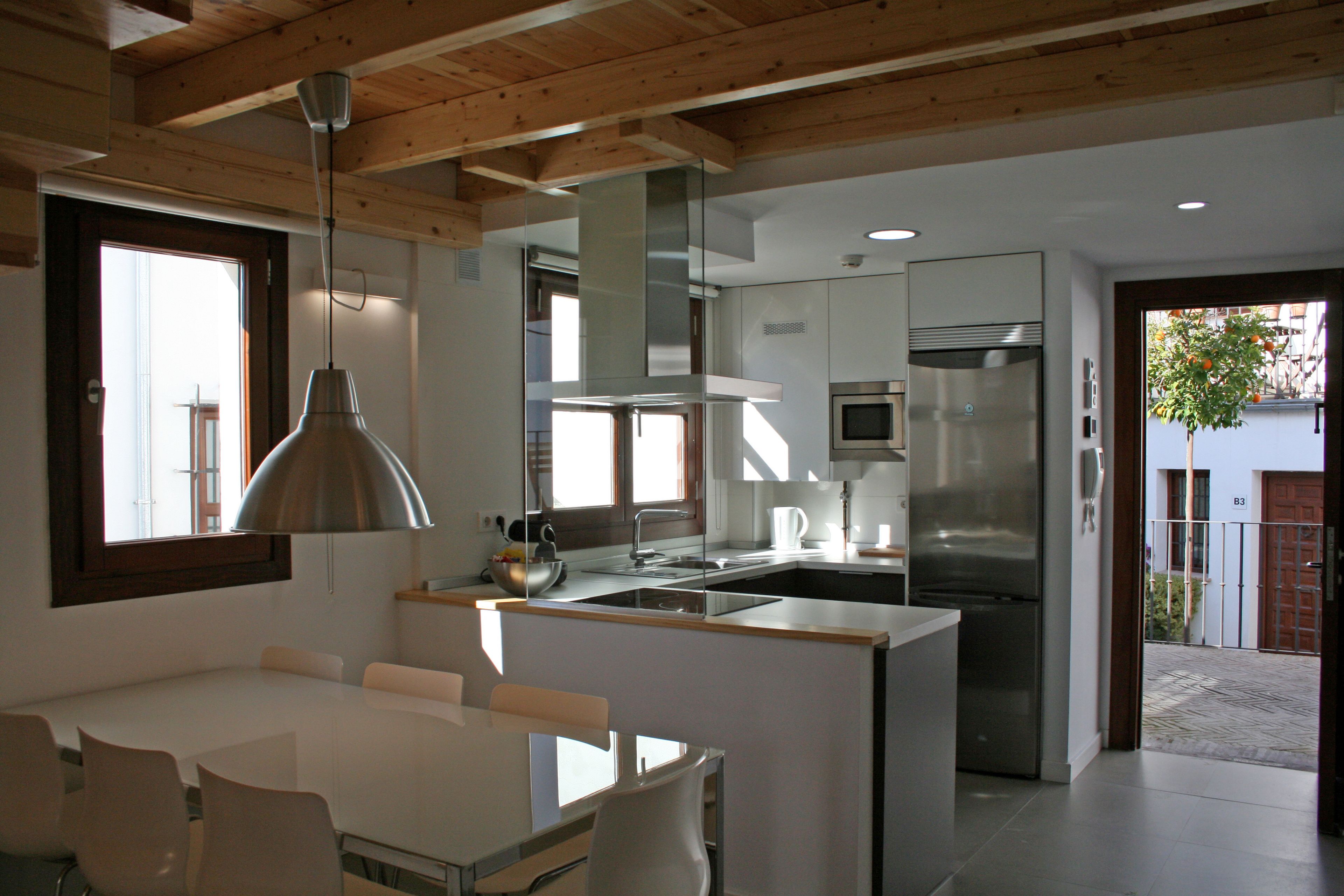 Una cocina moderna con una isla central, electrodomésticos de acero inoxidable y un comedor con una mesa y sillas blancas.