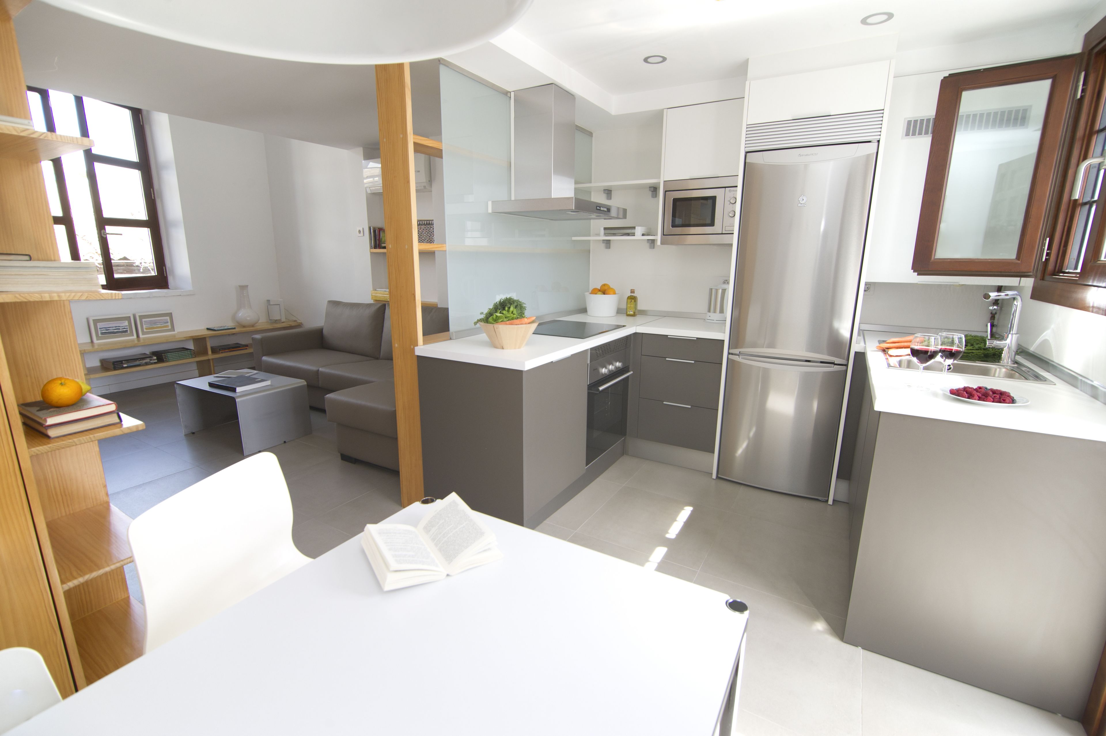 Una cocina compacta con electrodomésticos modernos, un comedor con mesa y sillas, y una pequeña sala de estar con sofá.