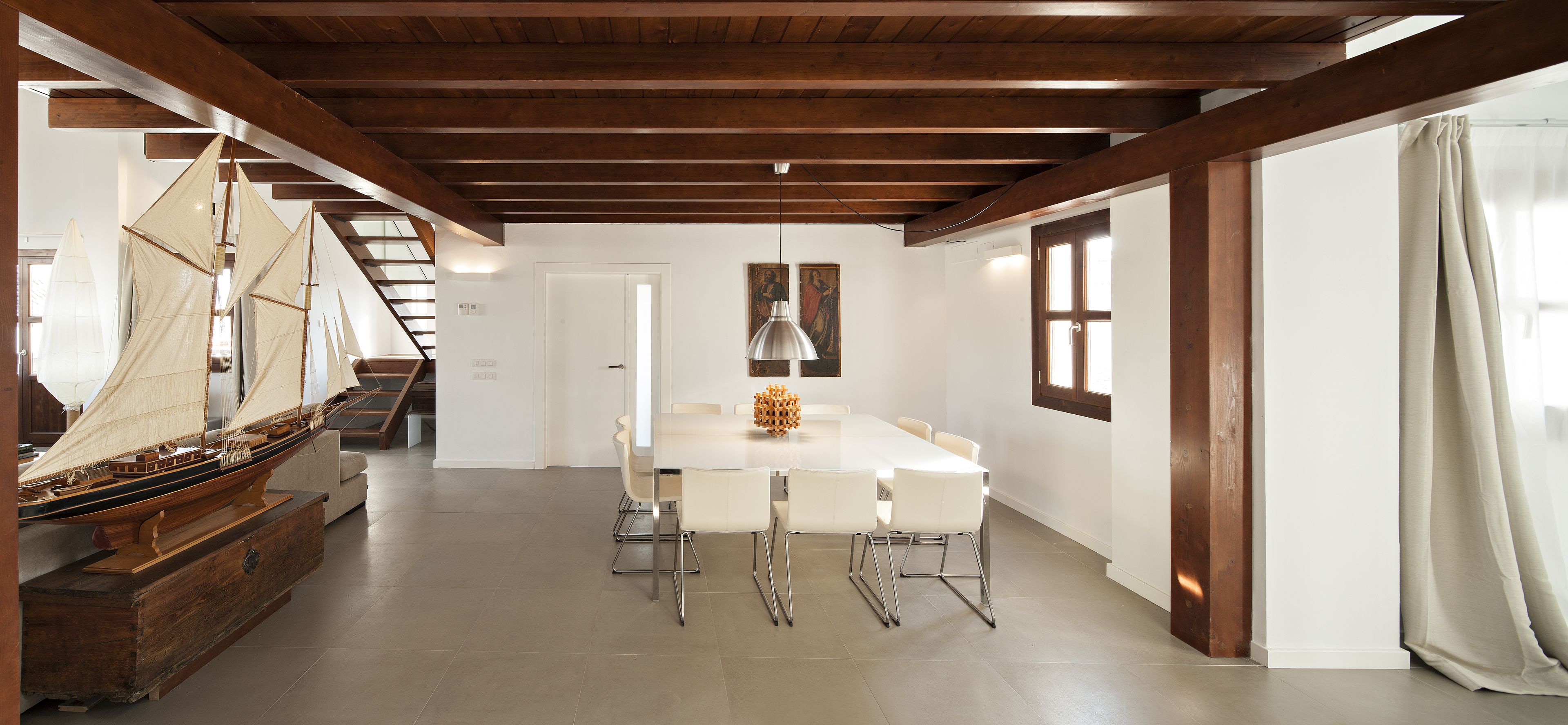 Un comedor amplio con una mesa larga, sillas blancas y techo de madera.