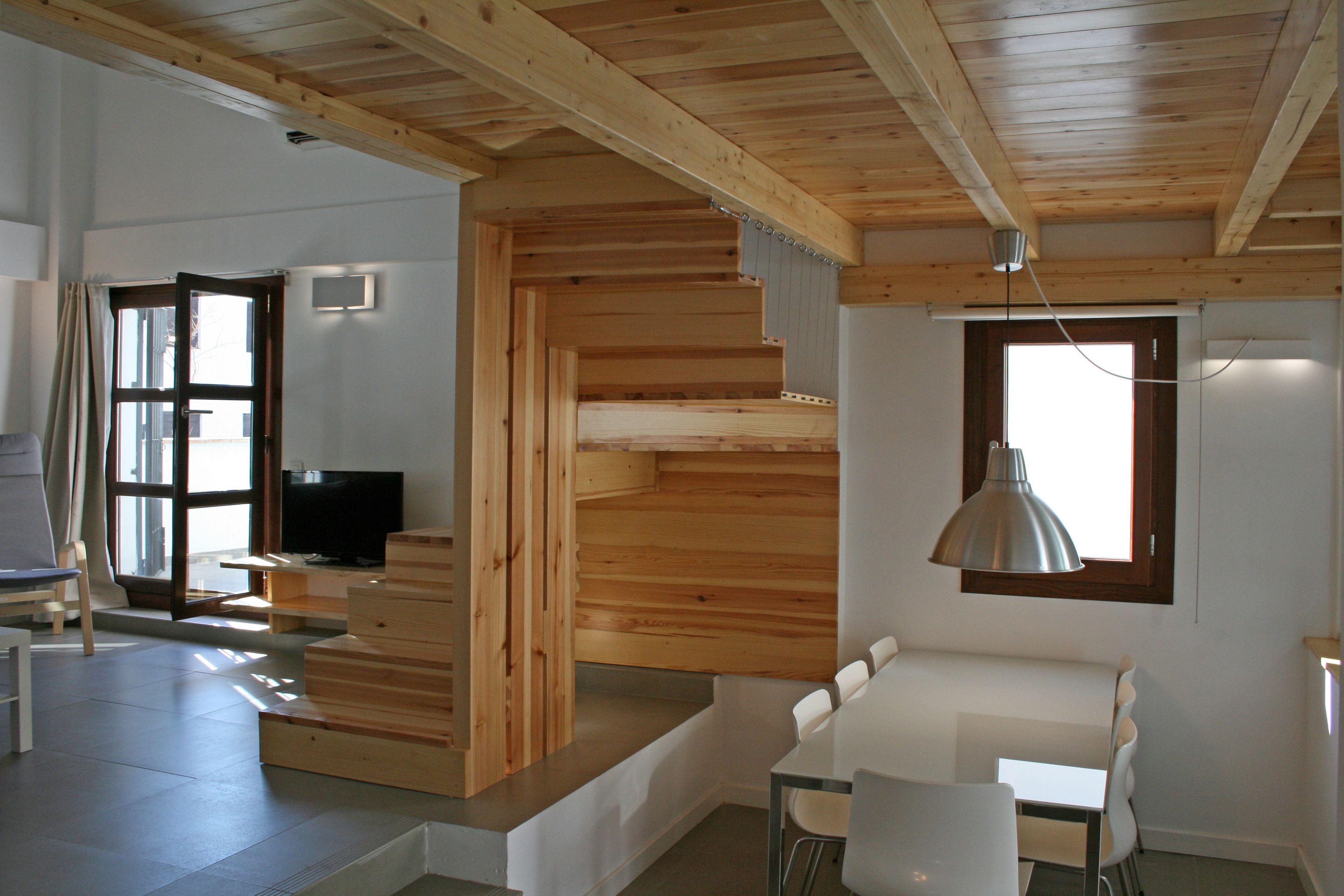 Een modern interieur met een houten trap, een eethoek met witte stoelen en een televisie in een hoek.