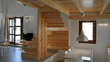 A modern interior with a wooden staircase, a dining area with white chairs, and a television in a corner.
