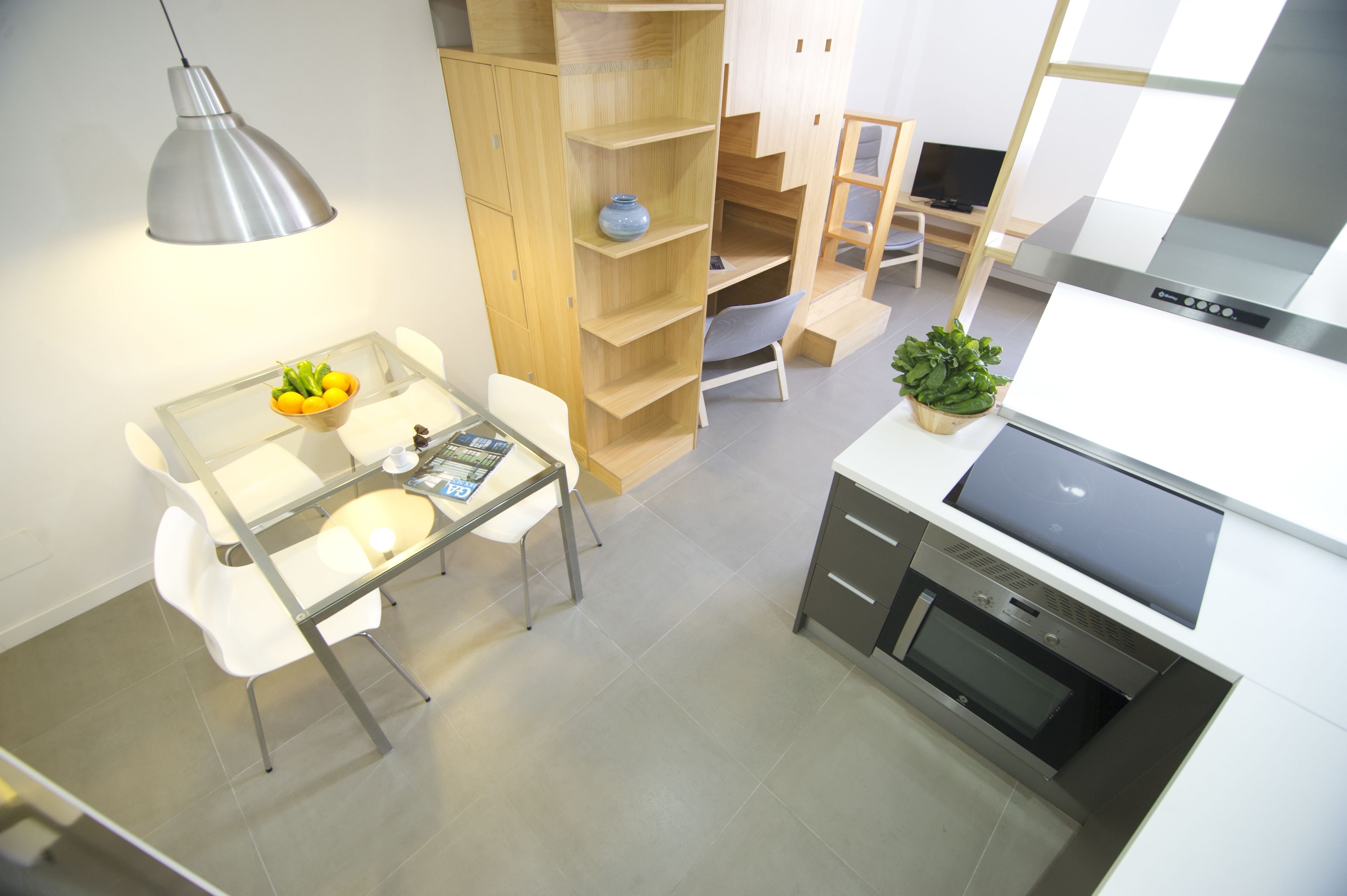 Una cocina moderna con horno empotrado, zona de comedor con mesa de vidrio y estantería de madera.