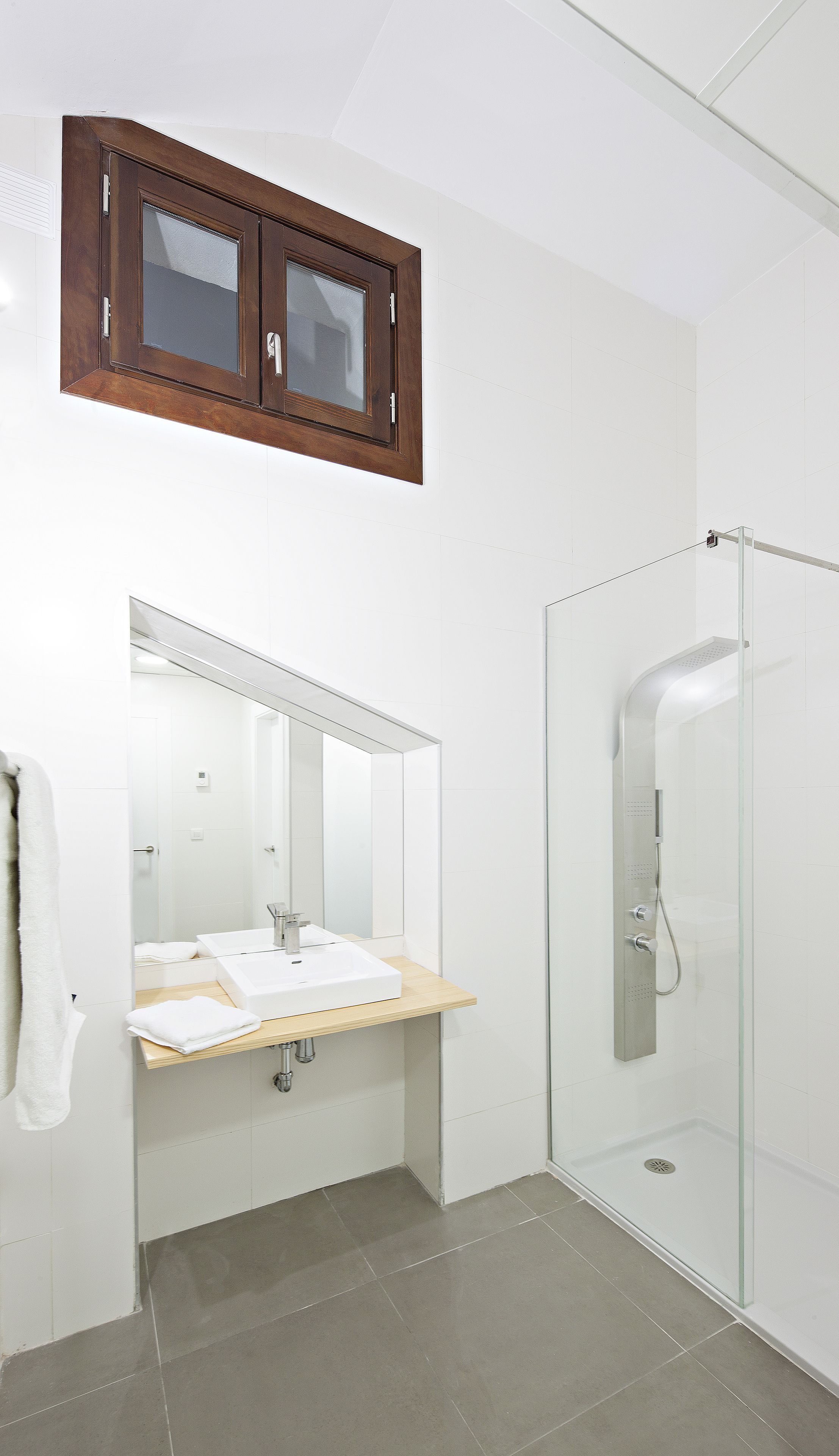 A modern bathroom with a wooden medicine cabinet, a large mirror, a sink with a wooden countertop, and a glass-enclosed shower.